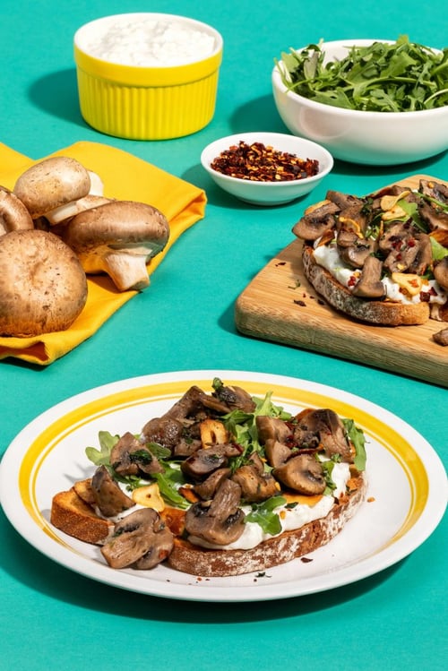 A plate with toast topped with cheese, mushrooms and arugula