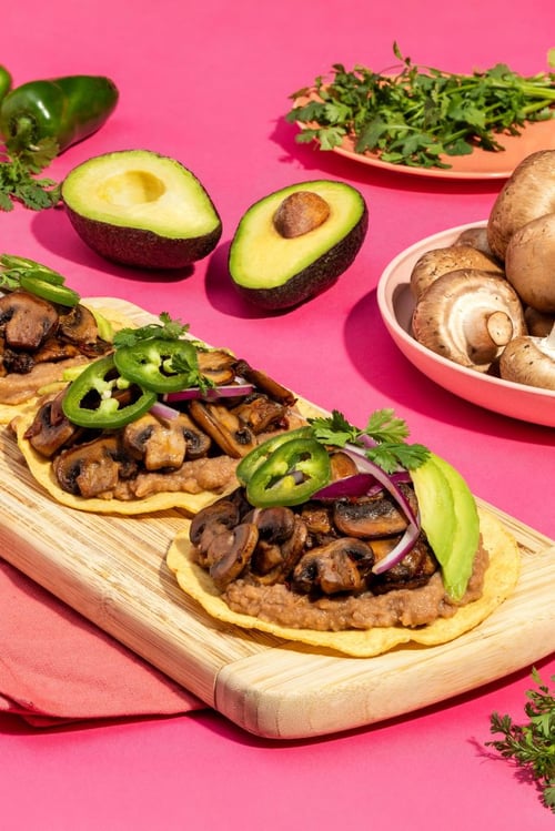 Tostadas with refried beans, mushrooms, red onions, cilantro, avocado, and jalapeños on top 