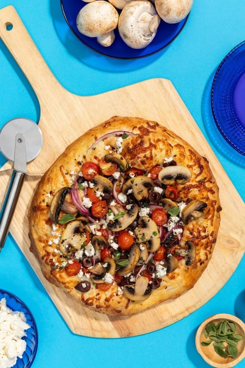 Mushroom Pizza on a cutting board with a pizza slicer and lots of veggies on top of pizza 