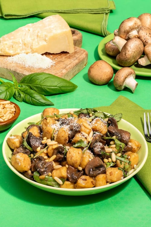 A bowl of gnocci with mushrooms, pine nuts, herbs and cheese on top