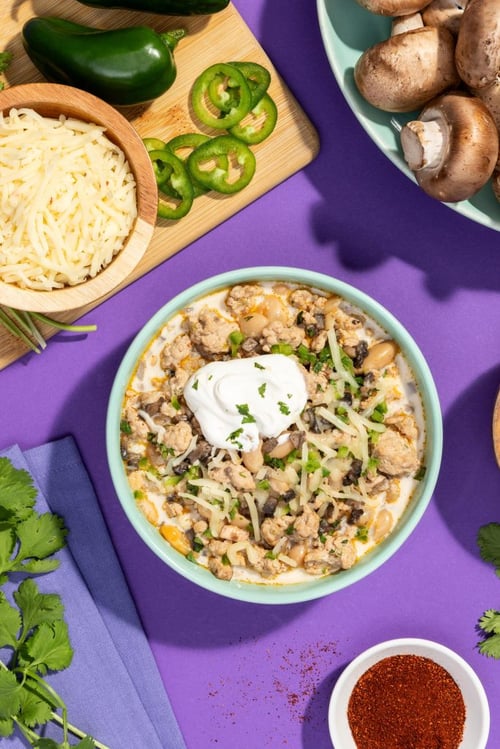 Bowl of white chili beans and mushrooms topped with sour cream, herbs and cheese