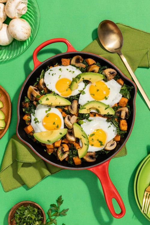 Mushroom breakfast skillet with sweet potatoes, kale and over easy eggs on top with avocado and cilantro 