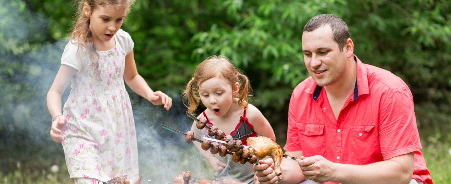 Father grilling mushroom skewers with two daughters